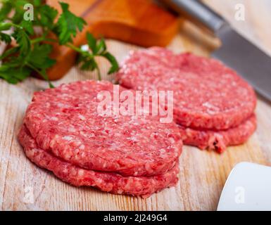 Cotolette di carne cruda con prezzemolo su tavola di legno Foto Stock