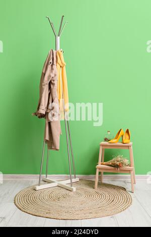Appendiabiti con giacca e sciarpa vicino al muro verde Foto Stock
