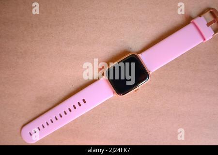 Orologio wireless Smart con cinturino rosa isolato su sfondo marrone in carta kraft. Foto Stock