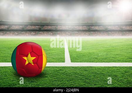 Calcio in uno stadio all'aperto luminoso con bandiera del Camerun dipinta. Fuoco su primo piano e sfera di calcio con profondità di campo poco profonda sullo sfondo Foto Stock