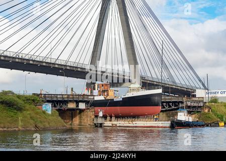 30 marzo 2022, Glebe Island Bridge, Sydney, Australia: La nave a vapore costiera del 1927, John Oxley che ha subito anni di restauro e conservazione è qui raffigurato sulla sua strada per essere finalmente refloated dopo 21 anni montato su un pontone presso i laboratori della Sydney Heritage Fleet a Roselle Bay. Dopo aver rimosso facilmente l'enorme ponte in cemento ANZAC, il pontone si adatta solo attraverso l'apertura del vecchio ponte dell'isola di Glebe sulla strada per un molo asciutto a Garden Island, più in basso nel porto di Sydney, dove sarà accuratamente rifocillato e testato. Foto Stock