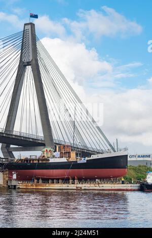 30 marzo 2022, Glebe Island Bridge, Sydney, Australia: La nave a vapore costiera del 1927, John Oxley che ha subito anni di restauro e conservazione è qui raffigurato sulla sua strada per essere finalmente refloated dopo 21 anni montato su un pontone presso i laboratori della Sydney Heritage Fleet a Roselle Bay. Dopo aver rimosso facilmente l'enorme ponte in cemento ANZAC, il pontone si adatta solo attraverso l'apertura del vecchio ponte dell'isola di Glebe sulla strada per un molo asciutto a Garden Island, più in basso nel porto di Sydney, dove sarà accuratamente rifocillato e testato. Foto Stock