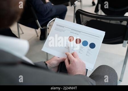 Le mani del giovane uomo d'affari che punta al cerchio beige nel documento finanziario mentre analizzano le informazioni durante la formazione Foto Stock