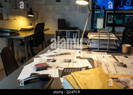 Parte del posto di lavoro del moderno agente fbi con documenti, prove, calcolatrice e telefono su scrivania illuminata da lampada in piccoli uffici Foto Stock
