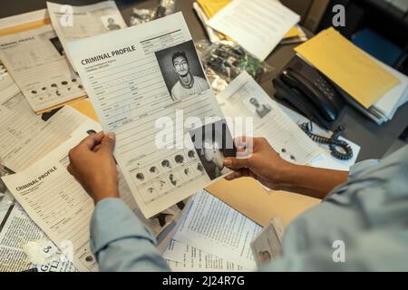 Mani di giovane agente FBI femminile in possesso di documento con dati personali di reato durante l'incarico di indagine in carica Foto Stock
