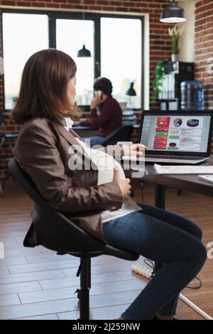 Donna d'affari che lavora sul grafico del diagramma finanziario dell'azienda, analizzando il rapporto delle statistiche per la presentazione. Donna incinta che guarda la crescita economica aziendale e la presentazione del progetto Foto Stock