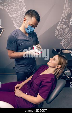 Dentista che seleziona il colore dei denti del paziente con comparatore digitale dei denti della guida dell'ombra Foto Stock