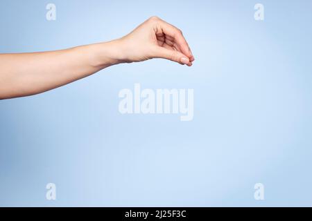 Gesto della mano della donna. La mano femminile posa come tenere o raccogliere qualcosa isolato su sfondo blu chiaro. Vista frontale Foto Stock