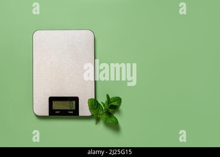 Bilance digitali da cucina e zuffo di menta fresco su sfondo verde. Spazio di copia. Apparecchio di misura per uso domestico per la dieta e la cottura. Bilance elettroniche. Foto Stock