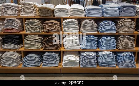 Pila di camicie colorate ripiegate sugli scaffali. T-shirt di colore toni terra sono accatastati. Foto Stock
