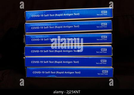 Scatole kit per test a flusso laterale NHS Covid-19 blu / kit per test per coronavrus con antigene a flusso laterale rapido su sfondo nero Foto Stock