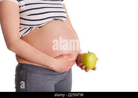 Donna incinta in piedi e tenendo la mela vicino al suo stomaco Foto Stock