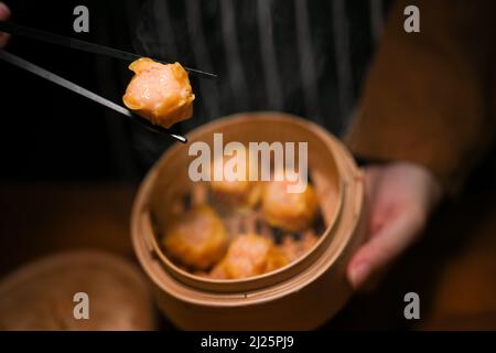 Immagine ravvicinata e messa a fuoco selettiva, Donna che mangia gnocchi di gamberi al vapore con bacchette e tiene un vaporetto di bambù. Informazioni Dim Sum Foto Stock