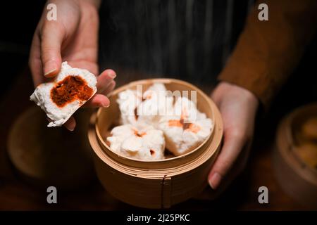 Primo piano, femmina che tiene o mangia panini di maiale cinese al vapore e tiene un vaporetto di bambù. Dim Sum Foto Stock