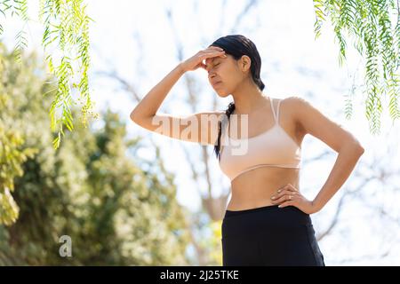 La giovane donna ispanica esprime un mal di testa mentre fa sport Foto Stock