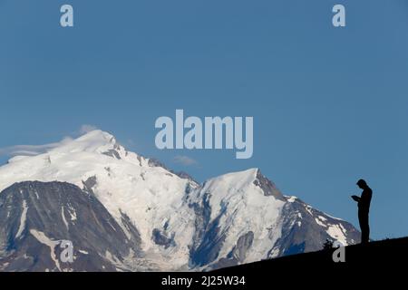 Massiccio del Monte Bianco in estate. Silhouette di uomo che legge la bibbia in natura. Meditazione. Foto Stock