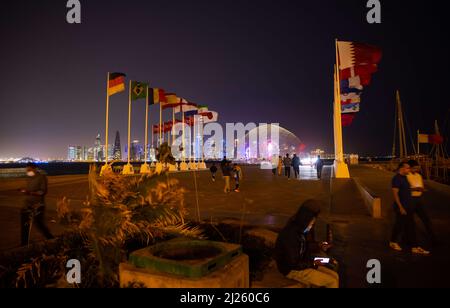 29 marzo 2022, Qatar, Doha: Le bandiere delle varie nazioni partecipanti sono viste su una piazza accanto al 'World Cup Countdown Clock' per la Coppa del mondo 2022 in Qatar sulla Corniche Promenade con lo skyline della West Bay di Doha. Doha ospiterà il Congresso FIFA il 31 marzo e l'estrazione della Coppa del mondo 2022 in Qatar il 1 aprile. Foto: Christian Charisius/dpa Foto Stock