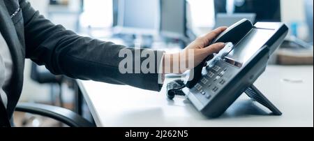 Primo piano della mano di un dipendente su un telefono fisso. La donna prende un telefono a pulsante sul posto di lavoro in ufficio Foto Stock