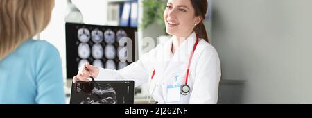 Ritratto di ginecologo sorridente che tiene l'immagine ecografica e mostra bambino piccolo Foto Stock