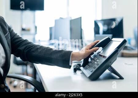 Primo piano della mano di un dipendente su un telefono fisso. La donna prende un telefono a pulsante sul posto di lavoro in ufficio Foto Stock