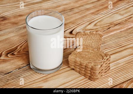 Un bicchiere di latte fresco e una pila di biscotti dolci su un tavolo di legno. Foto Stock