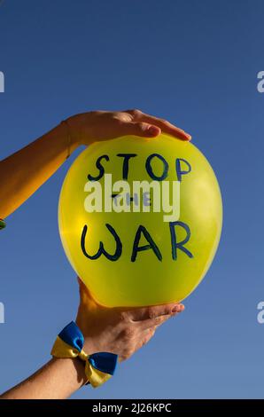 palloncino giallo con l'iscrizione fermare la guerra contro il cielo blu in mani femminili. Solidarietà con l'Ucraina. Ferma l'invasione militare russa di Ukr Foto Stock