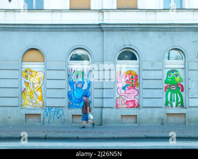 Praga, Repubblica Ceca-13 giugno 2015: Un uomo cammina lungo un muro con graffiti colorati nella strada, Una facciata edificio con graffiti su finestre ad arco Foto Stock