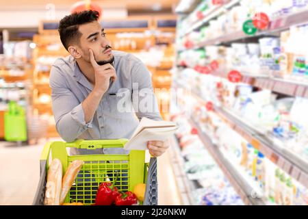 Uomo Arabo pensieroso fare acquisti di generi alimentari calcolare i prezzi nel supermercato Foto Stock