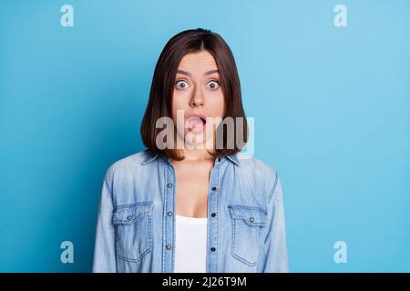 Foto di donna lucida impressionata indossare jeans camicia grandi occhi bocca aperta isolato blu sfondo di colore Foto Stock