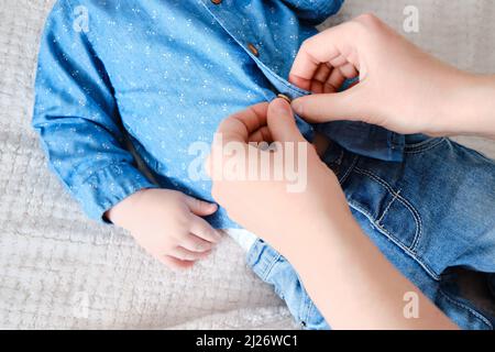 Una donna madre indossa una camicia blu a un bambino. La mamma indossa un bambino in abiti sul letto. Foto Stock