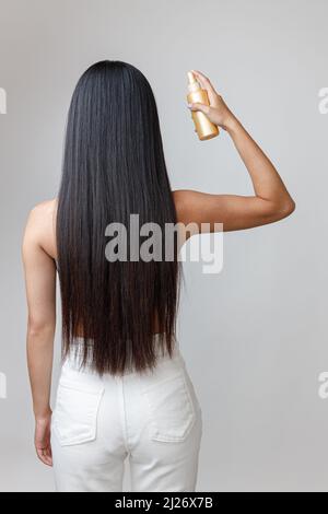 Brunette giovane donna spruzzando siero riparante sui capelli Foto Stock