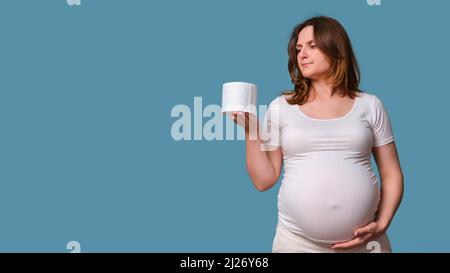 Ritratto di una donna incinta con carta igienica, sfondo blu Foto Stock