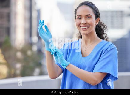 Prepararsi per un controllo. Shot di una giovane dottore donna che indossa guanti contro uno sfondo cittadino. Foto Stock