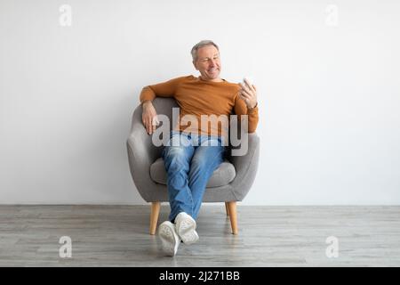 Ritratto di uomo maturo sorridente con smartphone seduto su poltrona Foto Stock