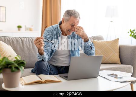 Uomo maturo e stanco seduto alla scrivania con il pc che massaggiano il nosebridge Foto Stock