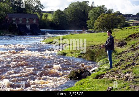 Un uomo che pesca la trota sul fiume Wharfe nello Yorkshire Dales vicino alla città mercato di Grassington. Lo Yorkshire Dales è un'area montana del P. Foto Stock