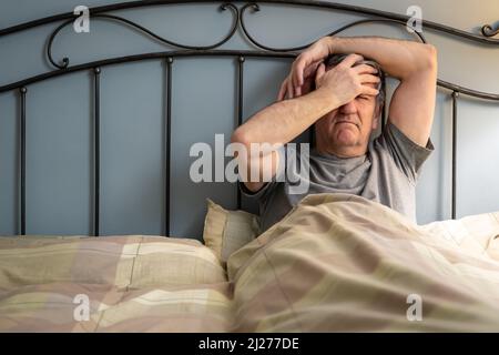 Uomo con insonnia seduta sul letto e con un gesto di disperazione. Foto Stock