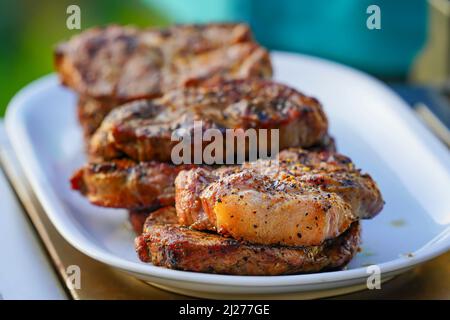 Bistecche di Juicy Burned Sizzle on con sale e Peperoni neri su piatto bianco per pranzo barbecue grigliato per picnic in estate. Foto Stock