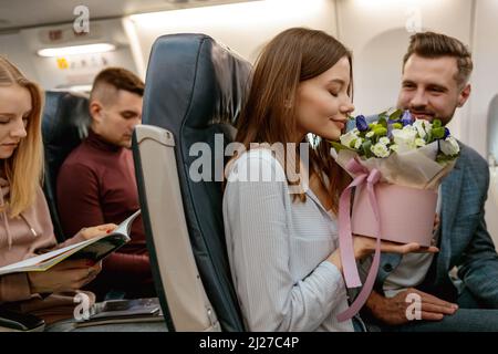 Giovane donna che odora fiori in aereo passeggeri Foto Stock