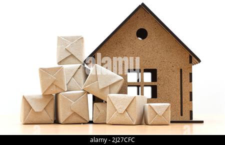 Mazzo di piccole confezioni di fronte ad un modello di casa in miniatura in piedi su un tavolo di legno su uno sfondo bianco. Foto Stock