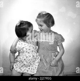 1961, hisotrical, due ragazze giovani dolci, sorelle, con sorrisi grandi, seduti a stretto contatto su uno sgabello per una foto di famiglia, Stockport, Manchester, Inghilterra, Regno Unito. Foto Stock