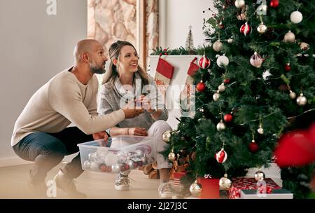 Potete mettere questo in su. Scatto corto di una coppia allegra di età media che mette le decorazioni su un albero di Natale all'interno a casa durante il giorno. Foto Stock