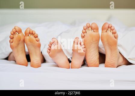 Tenere i piedi in alto. Shot di un irriconoscibile familys piedi posizionati l'uno accanto all'altro a letto mentre theyre dorme a casa al mattino. Foto Stock