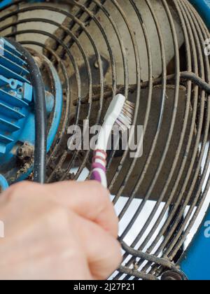 la ventola di estrazione dell'aria elettrica sporca viene pulita dai residui polverosi con una vecchia spazzola a denti Foto Stock