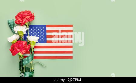 Composizione per le vacanze americane con bouquet di garofani e bandiera americana su sfondo verde con spazio copia. Tessera adatta per il Memorial Day, 4th o Foto Stock
