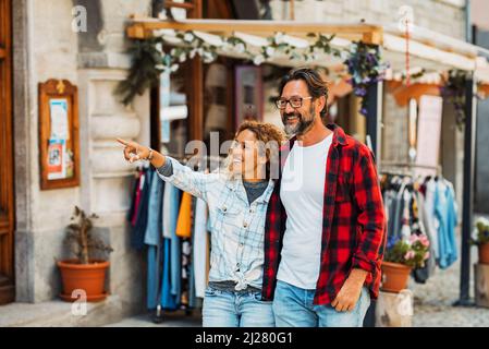 Coppia di giovani adulti felici godono di shopping e attività turistica all'aperto per il tempo libero in strada. L'uomo e la donna godono camminare vicino ai negozi sorridenti Foto Stock