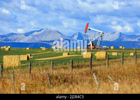 Un carro di perforazione per pickjack dell'industria petrolifera e del gas nelle praterie canadesi con le Montagne Rocciose canadesi ad Alberta, Canada. Foto Stock