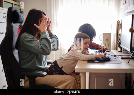 Donna stressata cercando di lavorare a distanza da casa con i suoi figli. Foto Stock