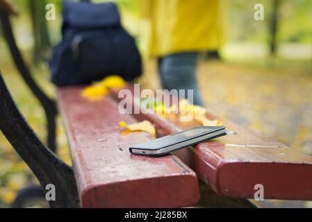 Smartphone dimenticato su una panca da parco. La donna sta lasciando da una panca dove ha perso il suo telefono cellulare. Foto Stock