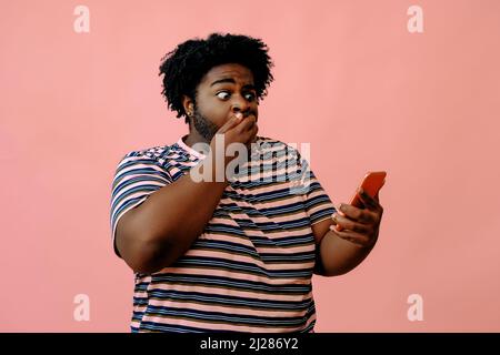 giovane uomo afroamericano con un telefono in posa in studio su sfondo rosa modello maschile in posa Foto Stock